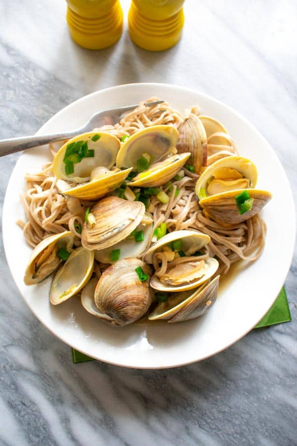 miso clams over buckwheat soba noodles on white round plate