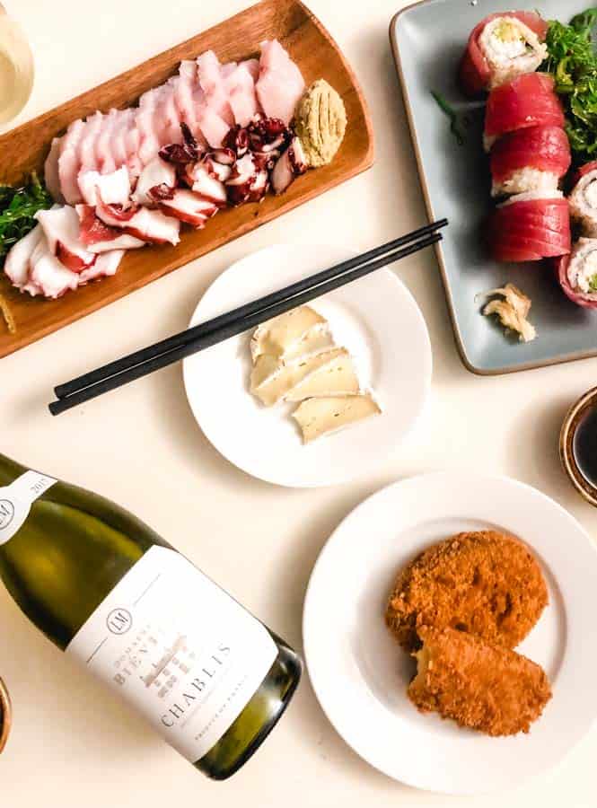bottle of chablis wine with sushi plates, brie cheese, and potato croquettes