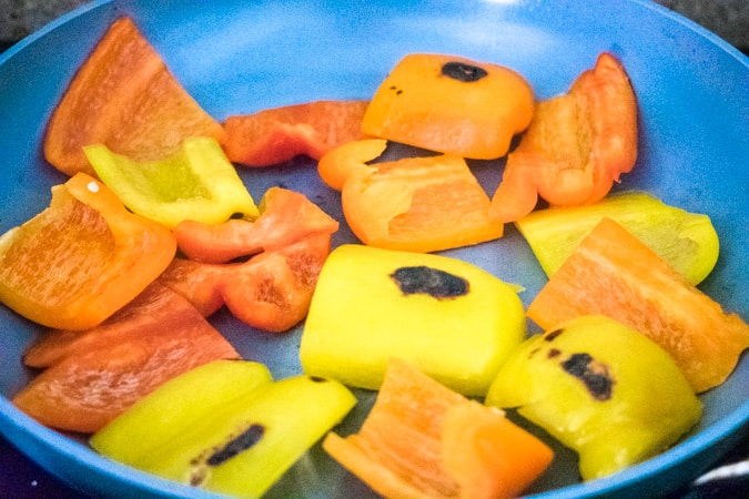 Mixed colored bell peppers searing in a gray nonstick pan.