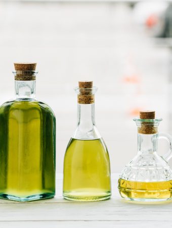 5 clear glass bottles of cooking oil in various heights and shapes, all with wooden corks.