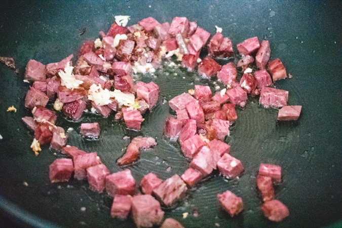 Chopped corned beef and garlic in a black wok.