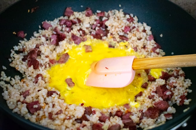 Scrambled eggs in the center of a wok with corned beef and rice around it. 