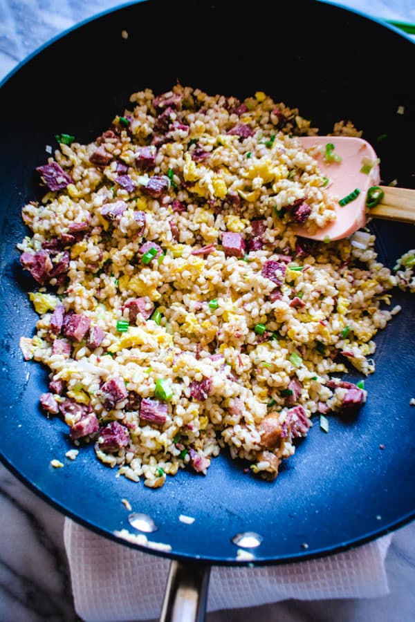Fried rice with corned beef and eggs in black wok with pink spatula.