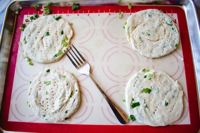 4 unbaked circles of scallion pancake on a baking sheet
