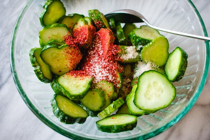 Sliced cucumbers in glass bowl with Korean red chili powder and sugar sprinkled on top.