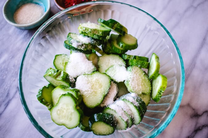 Glass bowl of sliced cucumbers with sea salt sprinkled on top.