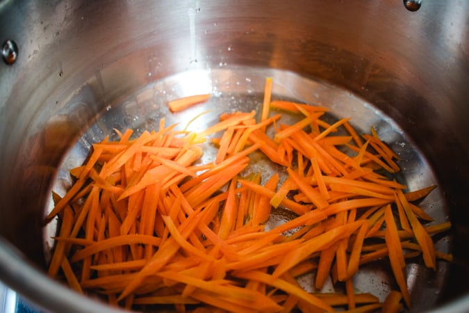 Julienned carrots in a pot with oil in a pan.