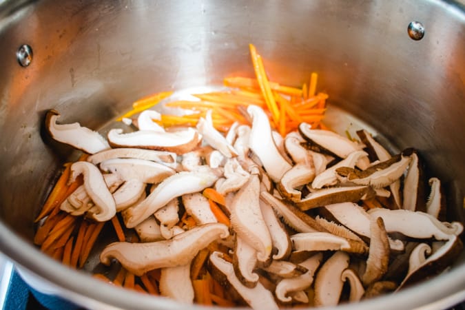 Sliced shitake mushrooms and carrots in a silver stock pot.