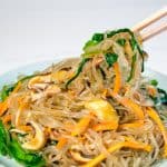 Korean glass noodle stir fry with vegetables on round blue plate with chopsticks.