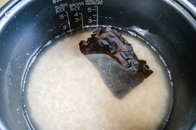 rice cooker with brown rice and a dried square of konbu