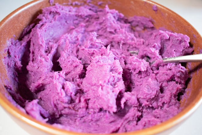Mashed purple yam in a brown bowl with a spoon
