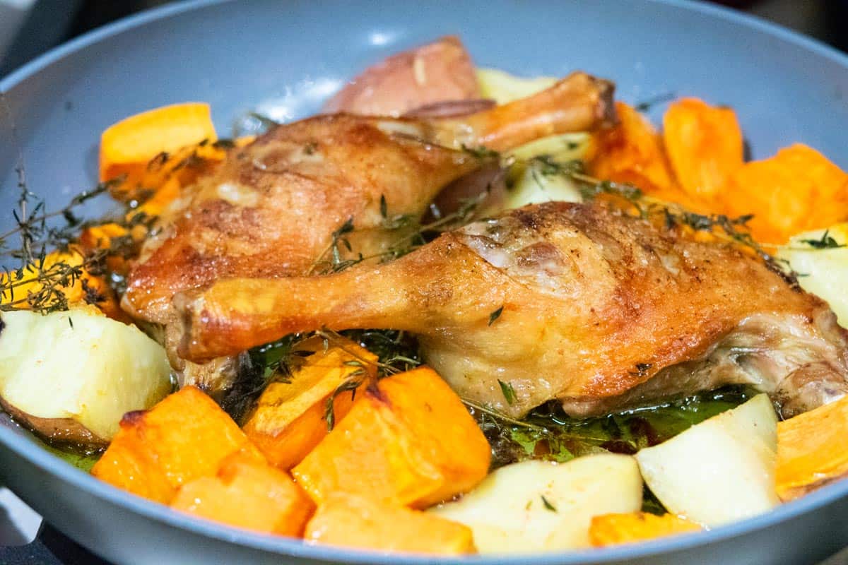 2 golden brown duck legs in a skillet with sweet potatoes