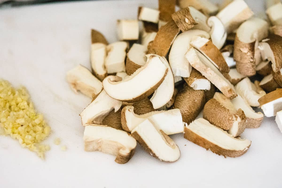 sliced shiitake mushrooms and minced garlic on a white cutting board