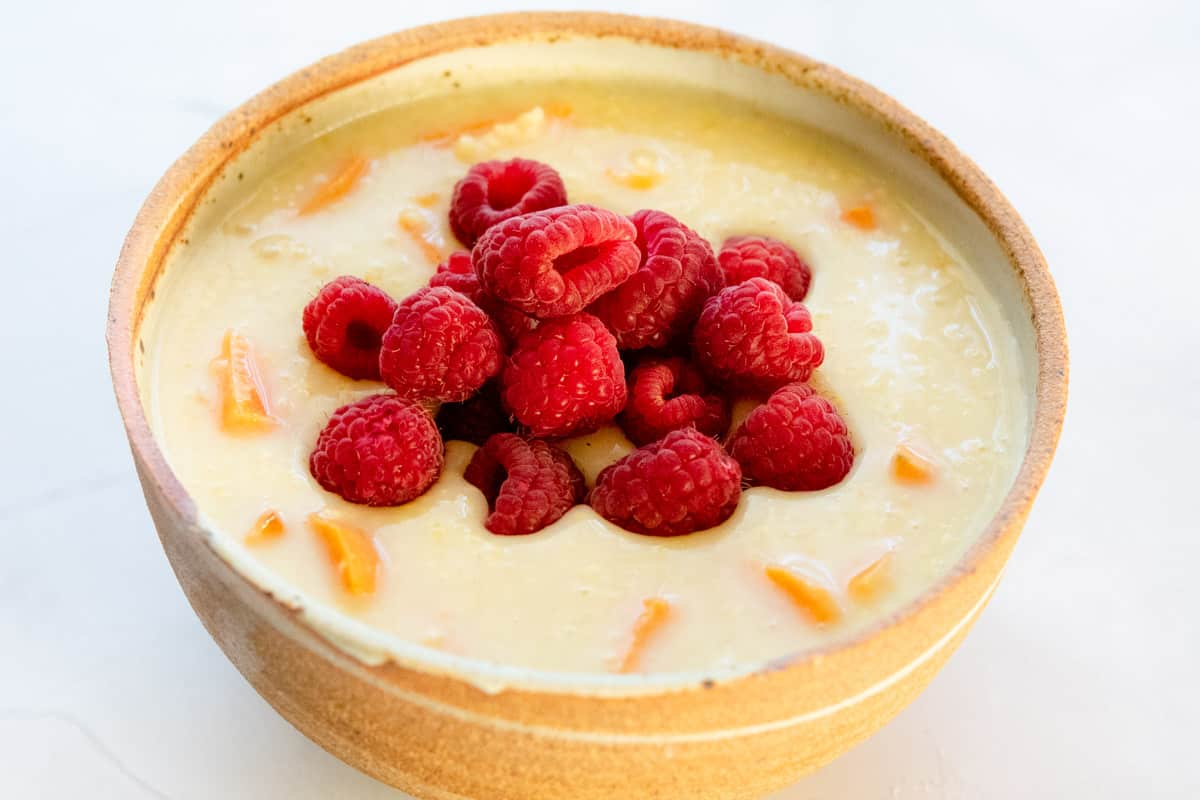 hot millet porridge in a bowl with mound of raspberries in the center